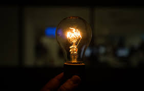 Lâmpada acesa sendo segurada por uma mão em ambiente escuro, simbolizando ideia, inovação e a importância da pesquisa de mercado no desenvolvimento de produtos.